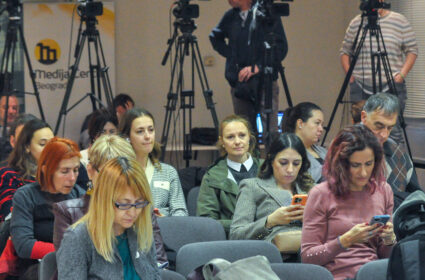 Media professionals sitting at a conference with cameras in the back of the room